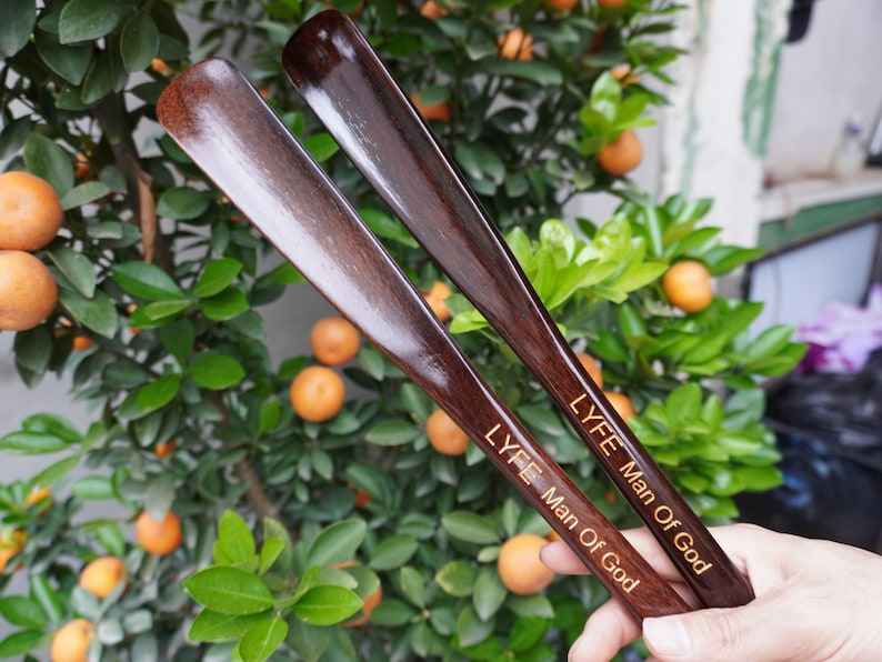Pode incluir: Duas cal&ccedil;adeiras de madeira castanho-escura com um acabamento liso e polido. Cada cal&ccedil;adeira apresenta o texto gravado LYFE Man Of God numa fonte de cor clara ao longo do cabo. Os artigos t&ecirc;m uma forma curva e alongada para cal&ccedil;ado.