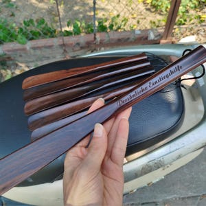 Pode incluir: Um conjunto de cal&ccedil;adeiras de madeira castanho-escura com um acabamento liso e polido. A cal&ccedil;adeira superior apresenta o texto gravado "Pers&ouml;nliche Einstiegshilfe" e inclui um pequeno cord&atilde;o preto no cabo para pendurar convenientemente.