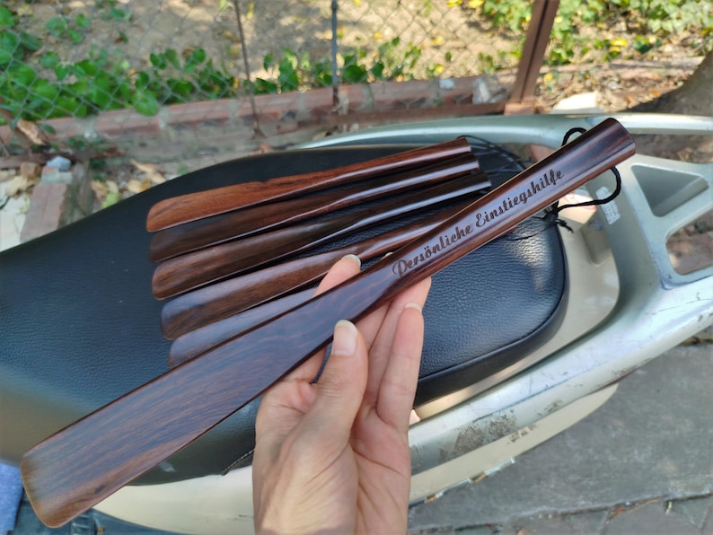 Pode incluir: Um conjunto de cal&ccedil;adeiras de madeira castanho-escura com um acabamento liso e polido. A cal&ccedil;adeira superior apresenta o texto gravado "Pers&ouml;nliche Einstiegshilfe" e inclui um pequeno cord&atilde;o preto no cabo para pendurar convenientemente.