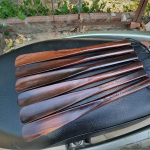 Pode incluir: Um conjunto de cinco cal&ccedil;adeiras de madeira polida com um design suave e curvo. Cada cal&ccedil;adeira apresenta um veio de madeira escuro e rico e est&aacute; presa a um cord&atilde;o preto fino. Duas cont&ecirc;m o texto em alem&atilde;o Pers&ouml;nliche Einstiegshilfe.