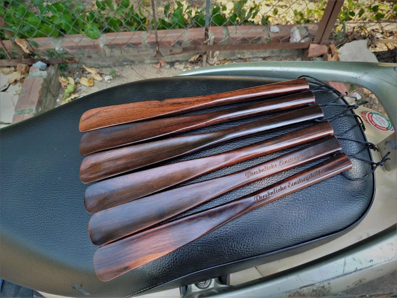 Pode incluir: Um conjunto de cinco cal&ccedil;adeiras de madeira polida com um design suave e curvo. Cada cal&ccedil;adeira apresenta um veio de madeira escuro e rico e est&aacute; presa a um cord&atilde;o preto fino. Duas cont&ecirc;m o texto em alem&atilde;o Pers&ouml;nliche Einstiegshilfe.