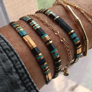 Peut inclure: Plusieurs bracelets et un bracelet chaîne en or sont présentés sur un poignet. Les bracelets sont ornés de perles noires, dorées et turquoise. Un bracelet a un design en forme de bambou. Les bracelets sont un mélange de matériaux et de styles.