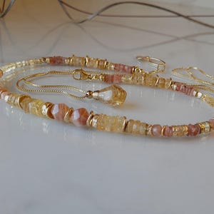 Peut inclure: Un collier à chaîne dorée avec un pendentif en pierre jaune à facettes et un rang de petites perles circulaires et plates alternées dans des tons de jaune translucide, orange pâle et pêche, agrémenté de petites entretoises en métal doré.