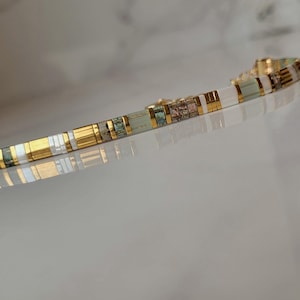 Puede incluir: Una pulsera delicada compuesta por cuentas rectangulares alternas en tonos verde salvia, blanco y oro met&aacute;lico. El dise&ntilde;o presenta un patr&oacute;n repetitivo de segmentos lisos de colores s&oacute;lidos intercalados con peque&ntilde;as cuentas texturizadas.