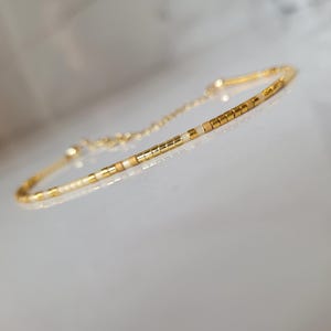 Op de afbeelding: Delicate goudkleurige armband met een reeks kleine, rechthoekige kralen in goud en gebroken wit. De armband heeft een fijne ketting en sluiting. Het ontwerp is eenvoudig en elegant, geschikt voor dagelijks gebruik of speciale gelegenheden.