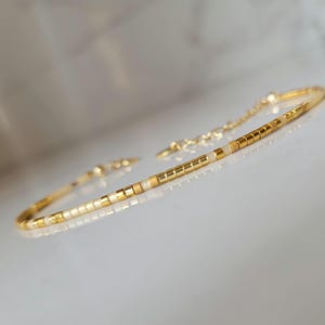 Op de afbeelding: Delicate goudkleurige armband met een herhalend patroon van kleine, rechthoekige gouden en witte kralen. De armband heeft een fijne ketting en een sluiting. Het ontwerp is minimalistisch en elegant, geschikt voor dagelijks gebruik of speciale gelegenheden.