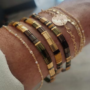 Peut inclure: Plusieurs bracelets dorés et perlés. Les bracelets présentent des chaînes dorées, de petites perles blanches et des perles rectangulaires dorées, vertes et noires. Différents styles de bracelets.