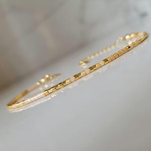 Peut inclure: Bracelet doré délicat avec des perles dorées et crème alternées. Le bracelet présente une chaîne fine et un design minimaliste, parfait pour un usage quotidien. Un accessoire élégant.