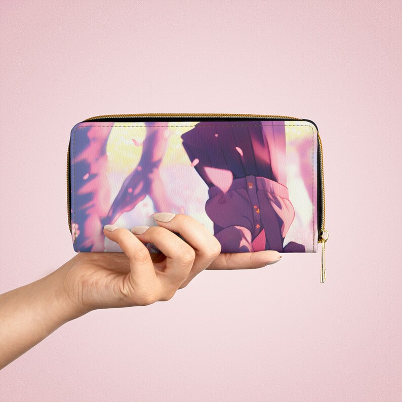 Puede incluir: Una cartera con cremallera rosa y morada con una ilustraci&oacute;n de estilo anime de dos personas de pie en un campo de flores rosas.