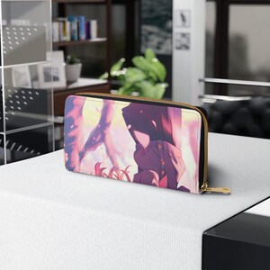 Puede incluir: Una cartera con cremallera rosa y morada con una ilustraci&oacute;n de estilo anime de dos personas de pie frente a un fondo rosa y amarillo.