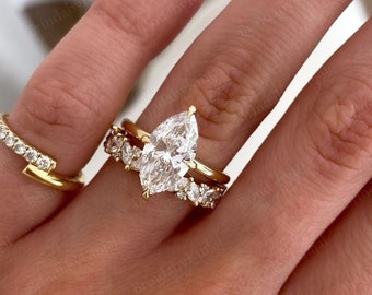 May include: A collection of gold rings, including a pear-shaped engagement ring with a halo of smaller stones and a curved band. The rings are set with clear gemstones. The image shows a close-up of the rings on a hand.