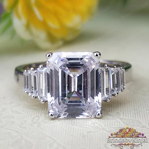 May include: A silver ring featuring a large, clear emerald-cut centre stone and smaller, clear baguette-cut stones on the band.
