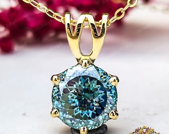 May include: A gold pendant necklace with a round, blue-green gemstone set in a prong setting. The pendant is attached to a delicate gold chain.