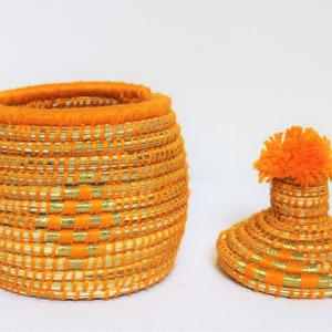Peut inclure: Un panier de rangement tiss&eacute; orange et or avec un couvercle assorti et un pompon orange moelleux sur le dessus.