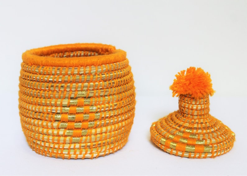 Peut inclure: Un panier de rangement tiss&eacute; orange et or avec un couvercle assorti et un pompon orange moelleux sur le dessus.