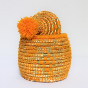 Peut inclure: Panier tiss&eacute; orange avec une bordure dor&eacute;e et un pompon orange moelleux sur le couvercle.