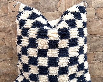 May include: A black and white checkered throw pillow with a fluffy texture. The pillow is made of a soft, woven material and has a square shape.