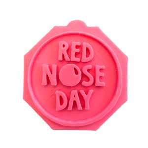 May include: A pink octagonal rubber stamp with the text "RED NOSE DAY" in white letters. The stamp has a raised red circle in the center.