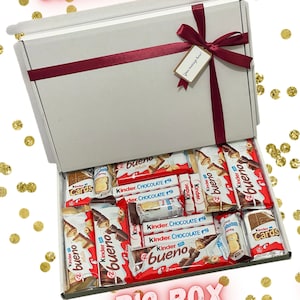 May include: A white gift box filled with assorted chocolate bars, including Kinder Bueno, Kinder Chocolate, and Kinder Cards. The box is tied with a red ribbon and a gift tag that says "Your message here!" The box measures 32 x 23 x 2 cm.