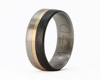 May include: A black and grey titanium ring with a gold band and a diamond logo engraved on the side.