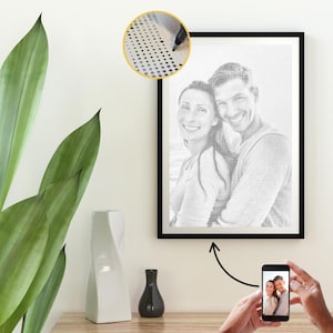 May include: A framed black and white portrait of a smiling couple, created with small dots. A close-up shows the dot-by-dot technique. A smartphone displays the original photo. A white vase and a black vase are on a wooden surface.