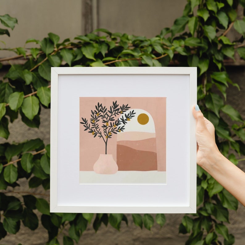 Pode incluir: Uma impress&atilde;o emoldurada branca com uma ilustra&ccedil;&atilde;o minimalista de uma pequena &aacute;rvore com frutos amarelos em um vaso rosa. O fundo &eacute; uma paisagem abstrata rosa e marrom com um sol amarelo.