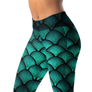 May include: Teal and black leggings with a mermaid scale pattern. The leggings feature a high waist and a repeating fan-shaped design in shades of teal and black. The fabric appears to be a stretchy material.