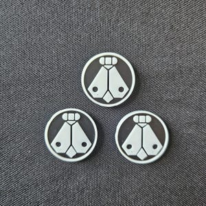 May include: Three circular, black and white decorative buttons. Each button features a white geometric design on a black background, with a white border. The buttons are arranged on a gray textured surface.