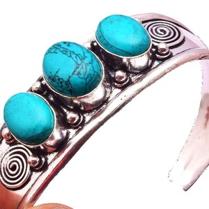 Könnte beinhalten: Ein silberfarbenes Armband mit drei ovalen Türkissteinen mit dunkler Maserung. Das Metallband ist mit geprägten Spiralmustern und kleinen kugelförmigen Akzenten verziert, die zwischen den Steinfassungen angebracht sind.