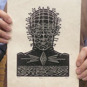 May include: A black and white linocut print depicting a character with pins in his head, a diamond shape, and a maze. The print is on textured paper and includes the word "Hell".