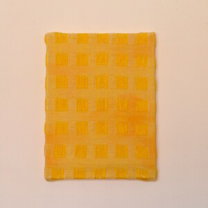 May include: A yellow square-shaped fabric with a checkered pattern. The fabric has a slightly textured surface.