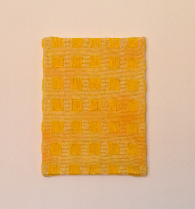 May include: A yellow square-shaped fabric with a checkered pattern. The fabric has a slightly textured surface.