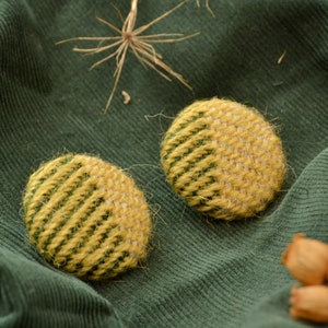 May include: Two round, yellow and green woven fabric buttons. The buttons are on a green corduroy fabric background.