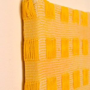 May include: A yellow woven wall hanging with a geometric pattern of squares. The hanging is made with a thick, textured yarn.