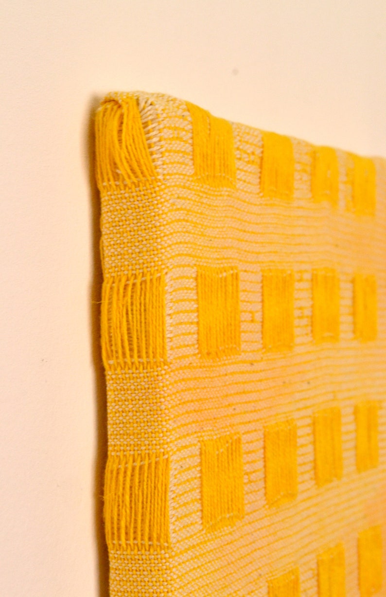 May include: A yellow woven wall hanging with a geometric pattern of squares. The hanging is made with a thick, textured yarn.