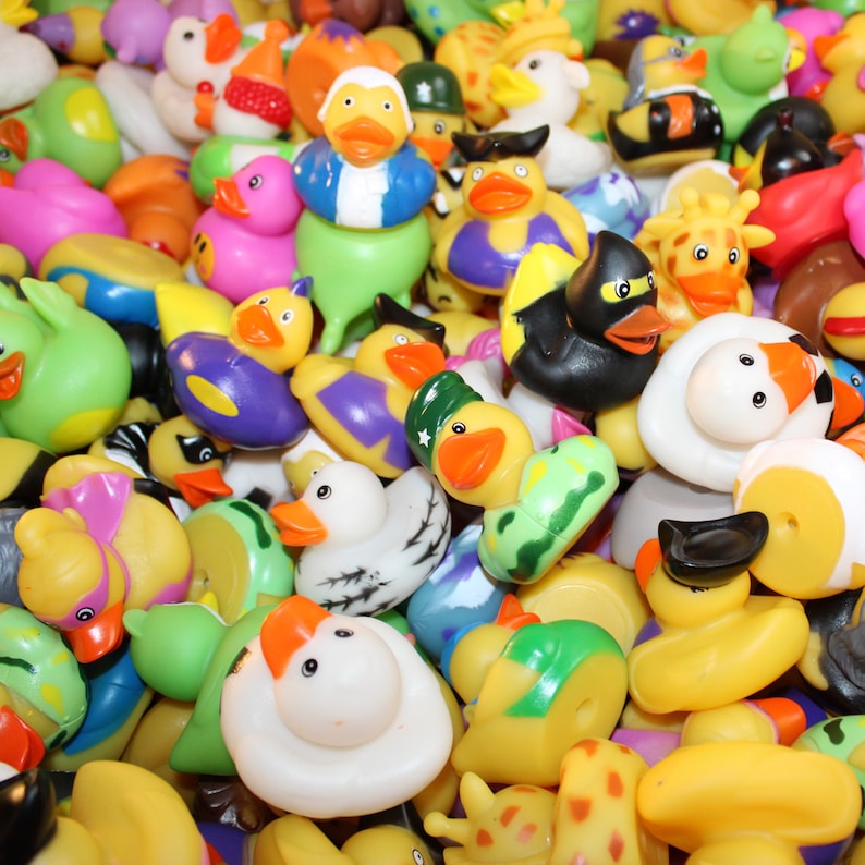 May include: A large collection of colorful rubber duck bath toys. The ducks are in various poses and designs, including a giraffe, a penguin, a turtle, and a duck wearing a hat.