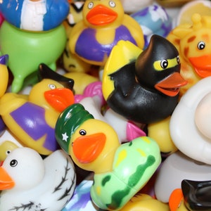 May include: A collection of colorful rubber duck toys, including a yellow duck with purple clothing, a black duck with a yellow beak, and a green duck with camouflage patterns.