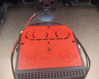 May include: A red and black 3D-printed device with the text "50 hrs" and "130 d". The device has a rectangular shape with a patterned grill and is connected to wires. The device is placed on a printer bed.