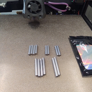 May include: A close-up of a group of silver metal rods on a brown surface. The rods are arranged in two groups of four and one group of three.