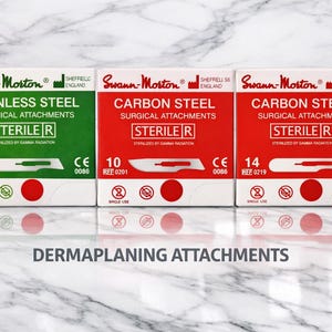 Peut inclure: Trois boîtes d'accessoires chirurgicaux Swann-Morton. Les boîtes sont étiquetées "Stainless Steel" et "Carbon Steel". Le texte "Sterile R" est visible sur chaque boîte. Le bas de l'image indique "DERMAPLANING ATTACHMENTS".