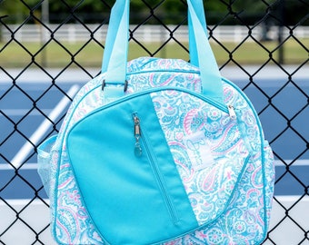 May include: A blue and white paisley patterned tote bag with a large zippered pocket on the front. The bag has two top handles and a mesh side pocket.