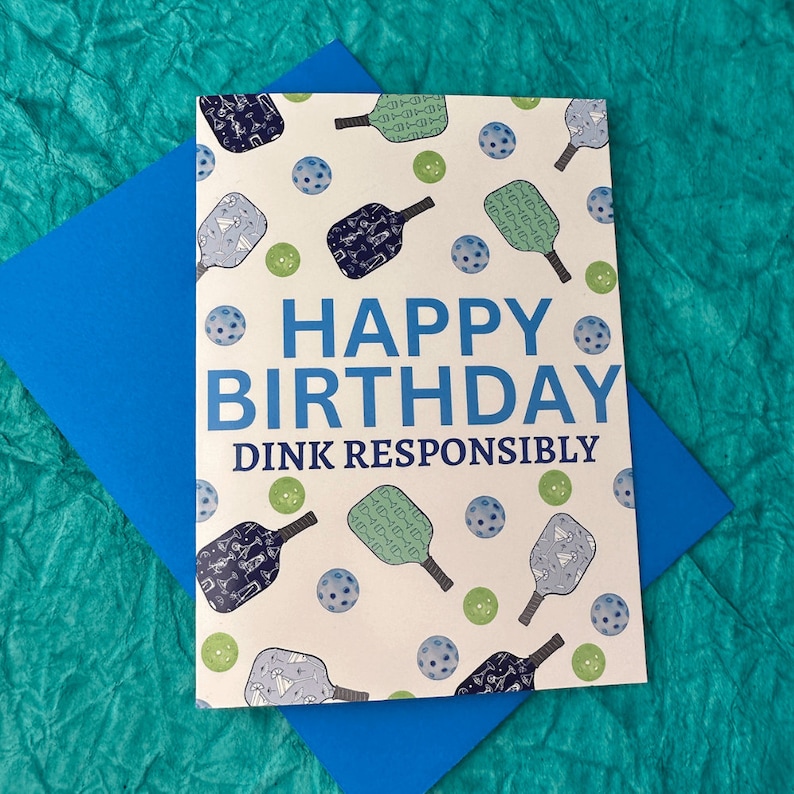 K&ouml;nnte beinhalten: Eine wei&szlig;e Karte mit einem blauen und gr&uuml;nen Paddleball-Design. Die Karte sagt "Happy Birthday Dink Responsibly".
