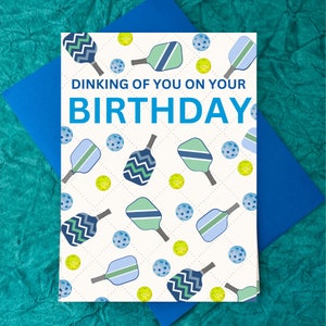 K&ouml;nnte beinhalten: Eine wei&szlig;e Geburtstagskarte mit einem blauen und gr&uuml;nen Paddelballmuster. Die Karte sagt "Dinking of you on your BIRTHDAY".