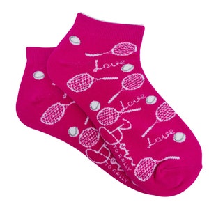 Puede incluir: Un par de calcetines tobilleros de color rosa brillante con un dise&ntilde;o de tenis. En los calcetines est&aacute;n impresas raquetas de tenis blancas, pelotas de tenis y la palabra "Love". Tambi&eacute;n est&aacute; impreso el texto "Born to Rally".
