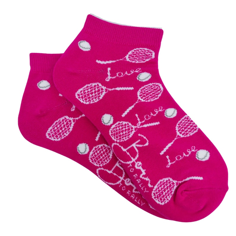 Puede incluir: Un par de calcetines tobilleros de color rosa brillante con un dise&ntilde;o de tenis. En los calcetines est&aacute;n impresas raquetas de tenis blancas, pelotas de tenis y la palabra "Love". Tambi&eacute;n est&aacute; impreso el texto "Born to Rally".