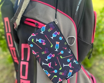 May include: A black golf accessory pouch with a zipper closure and a wrist strap. The pouch is patterned with colorful cocktail glasses, golf clubs, and the text "Let's Par Tee". The pouch is hanging on a golf bag.