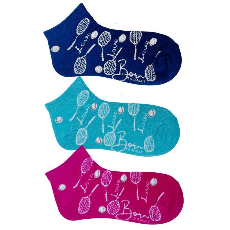 Puede incluir: Tres pares de calcetines tobilleros en azul, turquesa y magenta. Cada calcet&iacute;n presenta un tema de tenis con raquetas, pelotas y las palabras "Love" y "Born to Rally" en blanco. Los calcetines est&aacute;n hechos de un material suave y c&oacute;modo.