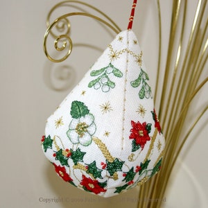 以下が含まれることがあります： 金、赤、緑の刺繍が施された、白い布製のクリスマスオーナメント。ホーリー、ヤドリギ、ポインセチアが刺繍されています。
