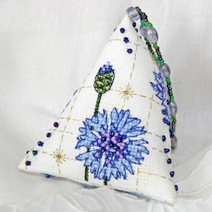 Pode incluir: Uma almofada triangular branca com um desenho de flor bordada em azul e verde. A almofada tem uma guarnição de contas em torno das bordas.