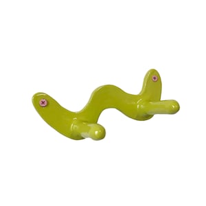 May include: A lime green ceramic wall hook with two hooks. The hooks are shaped like a wave and have pink screw heads.